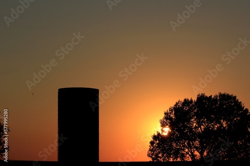 sunset out in the country in Kansas with a silo and tree silhouette's west of Hutchinson Kansas USA.