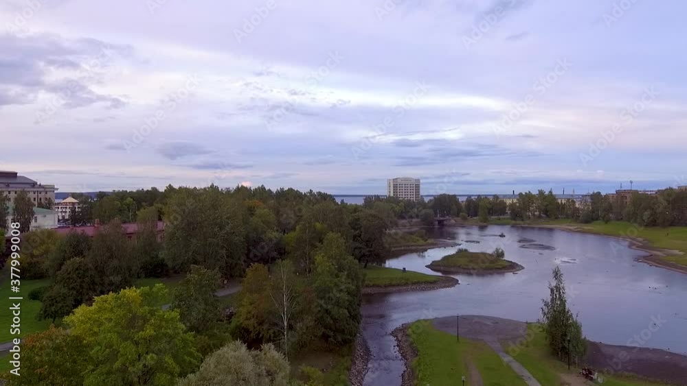 Aerial cityscape flying down above city park and river in autumn evening