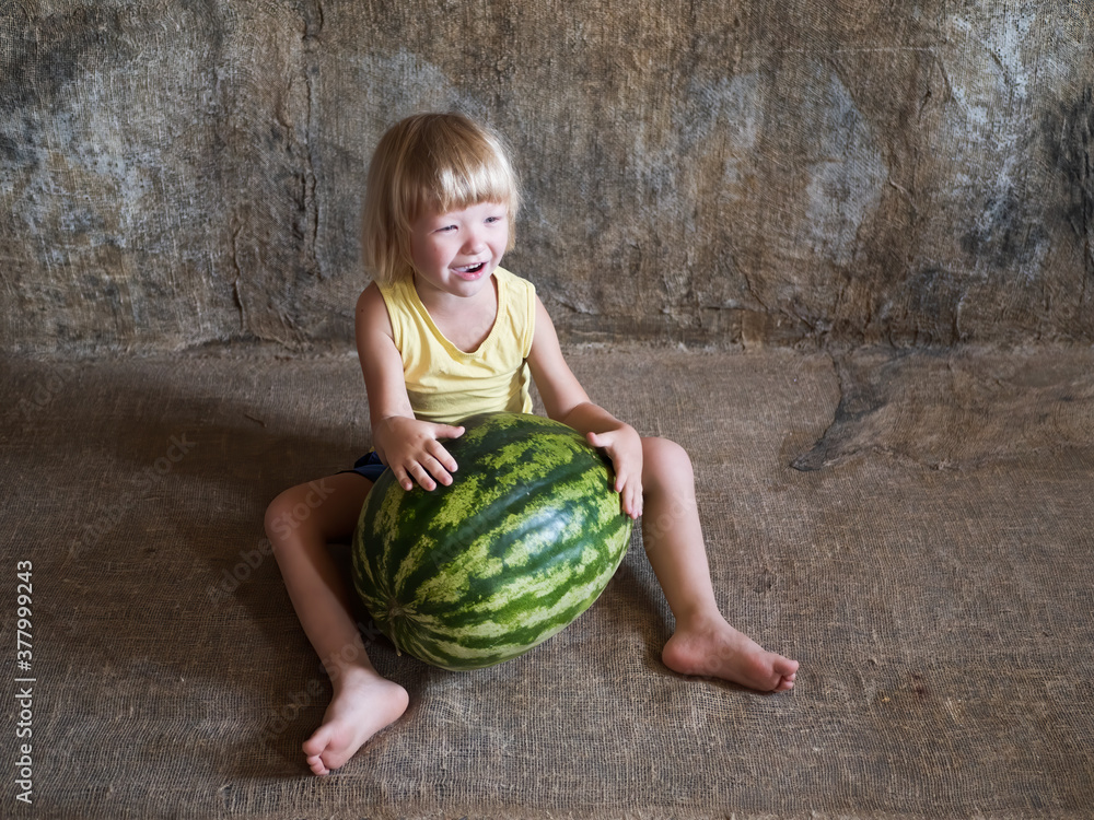 Fototapeta premium Funny blond boy sitting near big watermelon lying on floor