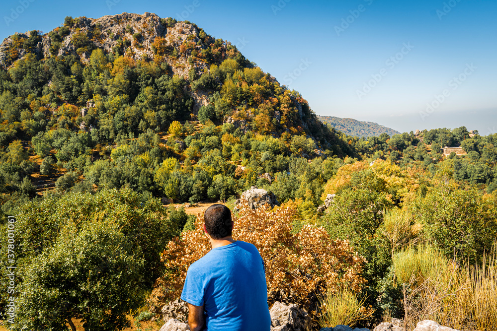 Young man sitting on top of cliff in summer mountains at sunrise and enjoying view of nature Young man sitting on top of cliff in summer mountains at sunrise and enjoying view of nature