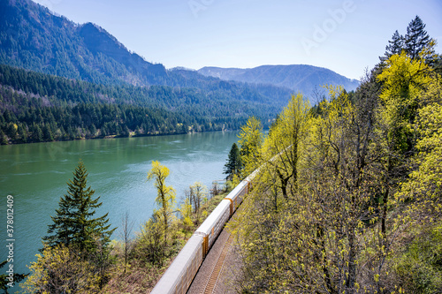 Freight train travels by rail along the Columbia River with a ridge of mountains on the opposite bank of the Columbia Gorge