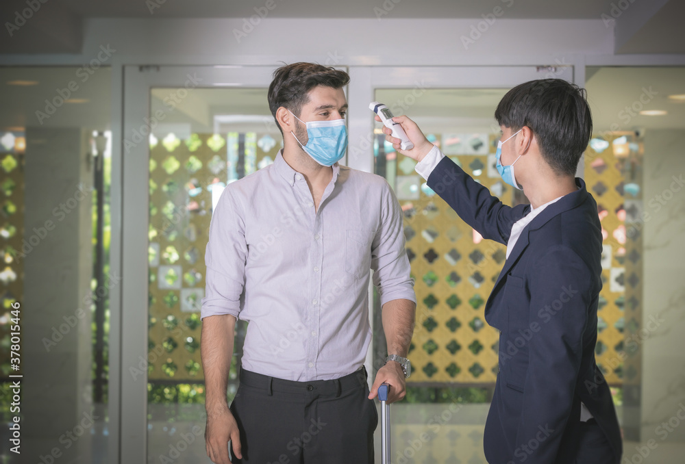 Body temperature check,Receptionist and guest wearing face mask at front desk while having conversation at hotel.Covid 19 and coronavirus infection protection and protective policy concept .