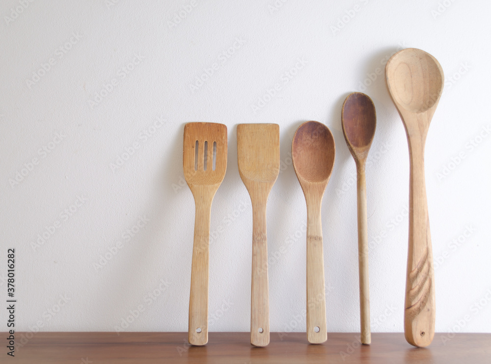 Five wooden spoons on wooden table against white wall. Five wooden spoons on wooden table against white wall.