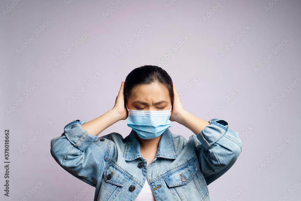 Asian woman wearing protective face mask and covering her ears by hands isolated over white background. Asian woman wearing protective face mask and covering her ears by hands isolated over white background.