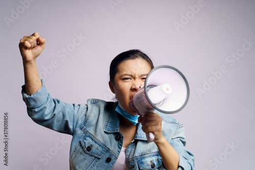 Asian woman wearing protective face mask shouting with megaphone isolated over white background.