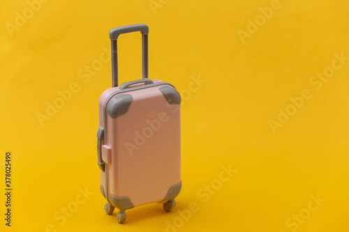 Travel or trip concept. Mini pink plastic travel suitcase on yellow background. Minimal style