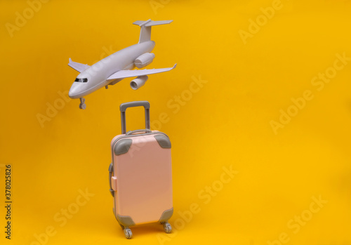 Air travel concept. Mini plastic travel suitcase, air plane on yellow background.