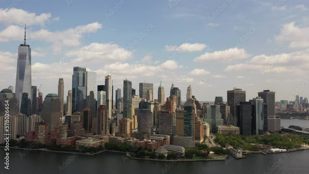 A bird's eye view over Upper Bay in New York where the drone camera tilts down showing lower Manhattan and the Hudson River. It is a sunny day with blue skies and white clouds. A bird's eye view over Upper Bay in New York where the drone camera tilts down showing lower Manhattan and the Hudson River. It is a sunny day with blue skies and white clouds.