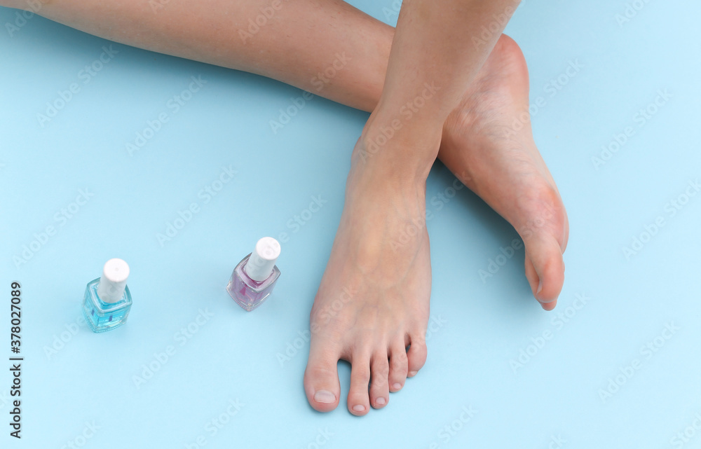 Female bare feet, nail polish bottle on blue background. Beauty Care Concept Female bare feet, nail polish bottle on blue background. Beauty Care Concept