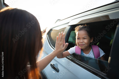 Back to school. Asian pupil girl with backpack sitting in the car waving goodbye to her mother to get ready to school.