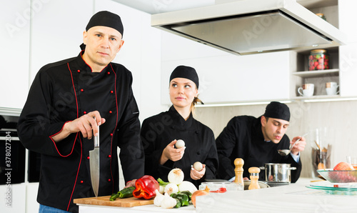 Team of woman and man chefs in black uniform preparing food on kitchen