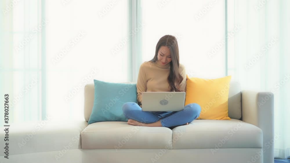 Relaxed Asian woman using her laptop computer sitting on the bed with her legs crossed, she is typing a message on the laptop keyboard and suddenly wins the prize, lottery, exited face expression Relaxed Asian woman using her laptop computer sitting on the bed with her legs crossed, she is typing a message on the laptop keyboard and suddenly wins the prize, lottery, exited face expression