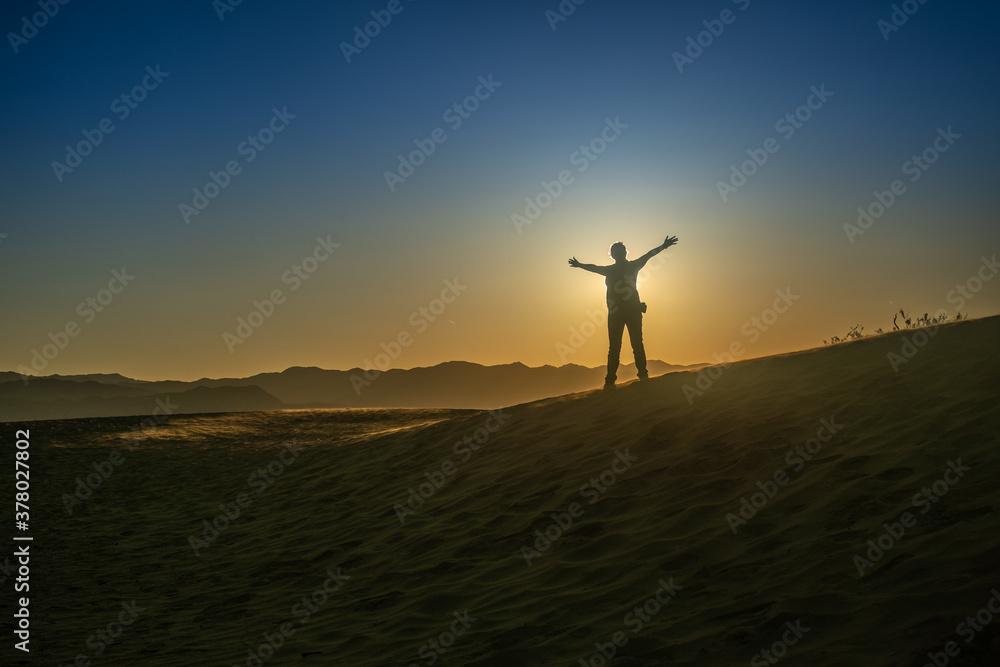silhouette of person standing in front of the sun on a hill at sunset with open arms in expression of freedom