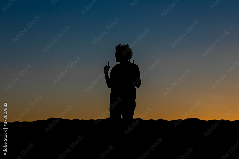 silhouette of a person standing on a hill looking in profile index fingers raised as an expression