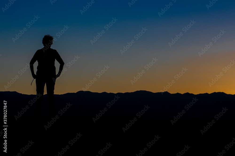 silhouette of a woman from the front with her arms on her hips in a sunset with the sky divided by yellow and blue