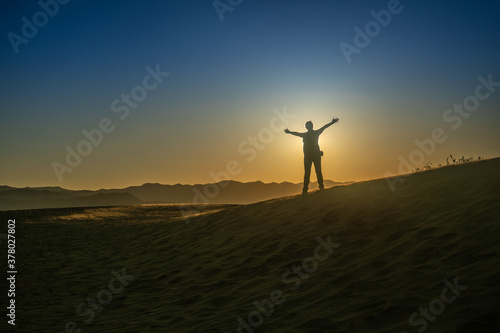 silhouette of person standing in front of the sun on a hill at sunset with open arms in expression of freedom