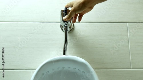 Hands pressing button on white ceramics urinal in toilet to flush urine and water flowing with ambient sound. photo