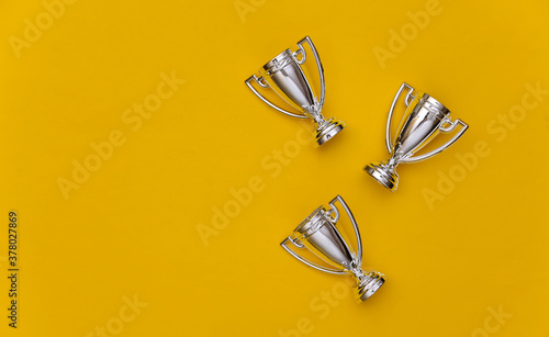 Mini silver sports championship cups on yellow pastel background. Copy space. Sport minimalism. Top view