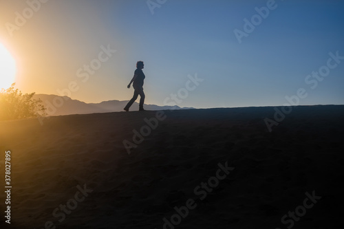 silhouette of a woman climbing a desert hill in a sunset