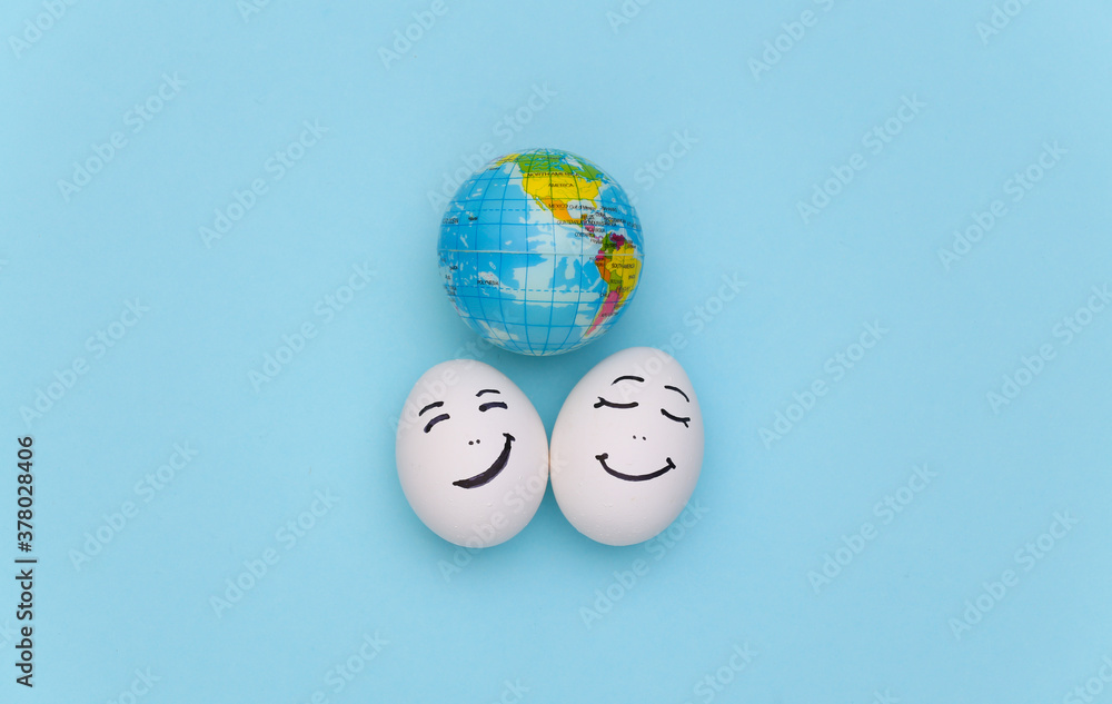 Happy couple of chicken eggs faces and globe on blue background. Earth Day