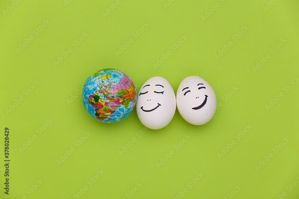 Happy couple of chicken eggs faces and globe on green background. Earth Day