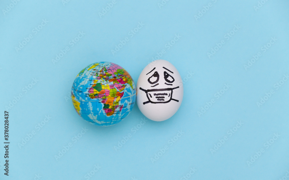The egg face in a medical mask and globe on blue background. Covid-19 pandemic. Top view