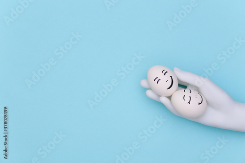 Mannequin hand holding Happy loving couple of chicken eggs faces on blue background