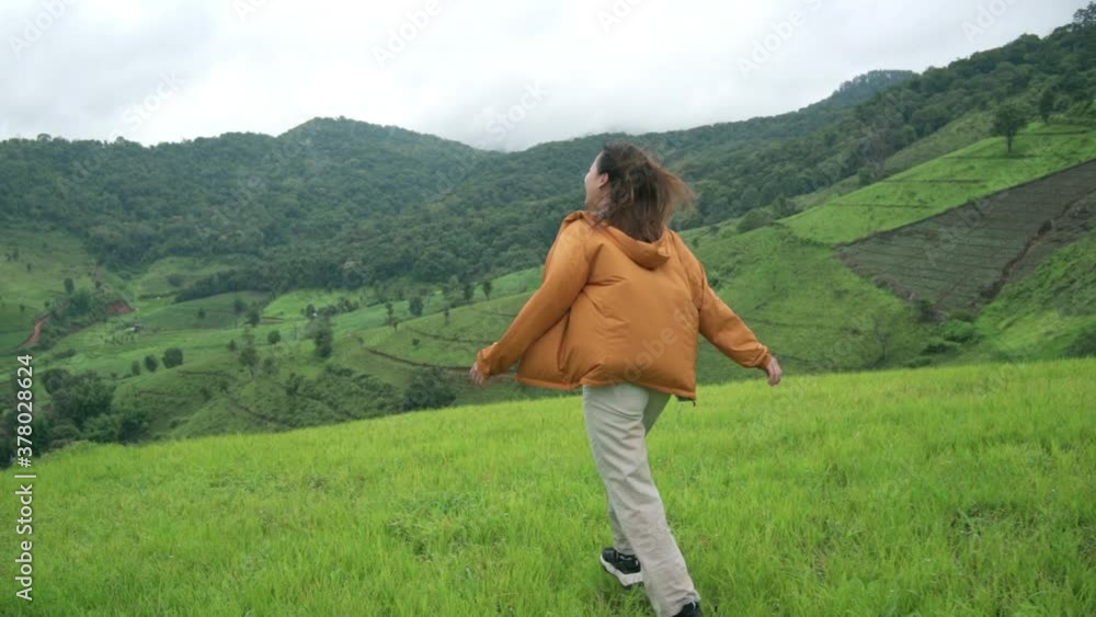 Happy young beautiful woman in yellow jacket walking on mountain peak with wind blowing through. Beautiful girl feel freedom and enjoy hiking on the hill. Outdoor lifestyle and nature travel concept. Happy young beautiful woman in yellow jacket walking on mountain peak with wind blowing through. Beautiful girl feel freedom and enjoy hiking on the hill. Outdoor lifestyle and nature travel concept.