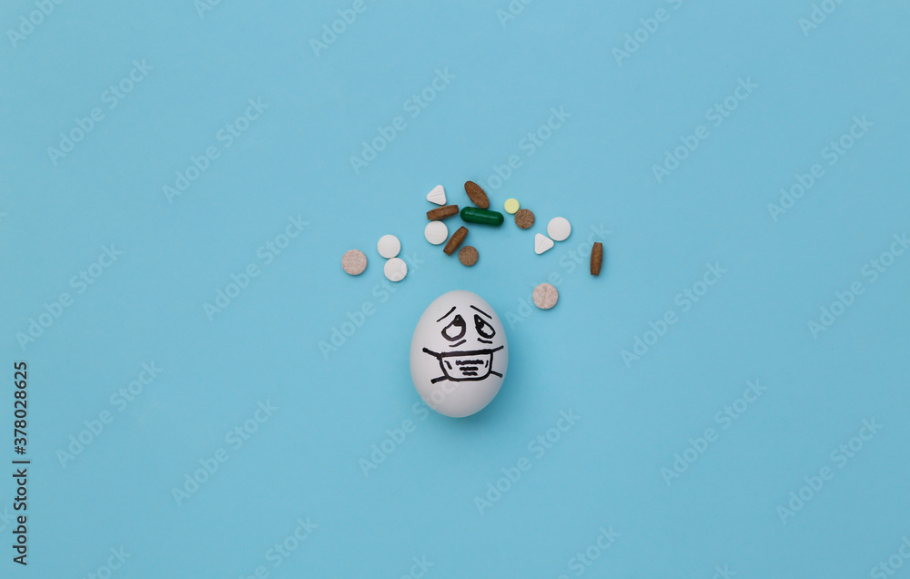 The egg face in a medical mask and pills on blue background. Covid-19 pandemic. Top view
