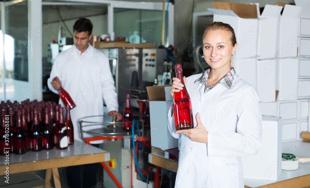 Two cheerful colleagues holding newly produced bottles of wine on winery manufactory