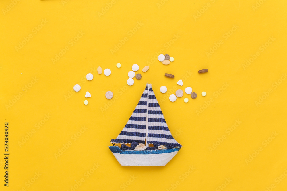 Treatment of seasickness. Sailboat and bottle of pills on yellow background. Top view - obrazy, fototapety, plakaty 