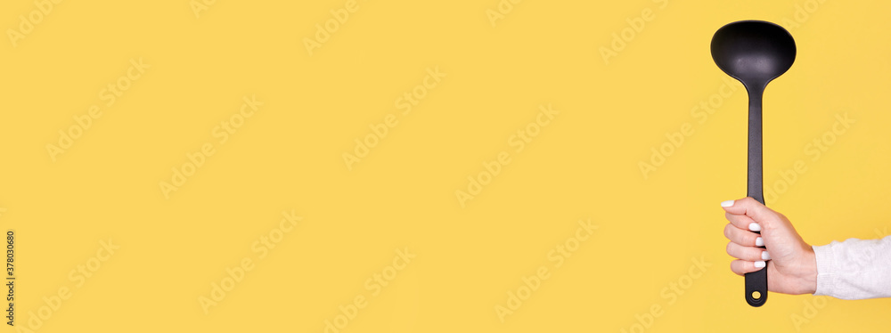 Black plasic ladle in hand, isolated on yellow background, copy space template, banner. Black plasic ladle in hand, isolated on yellow background, copy space template, banner.