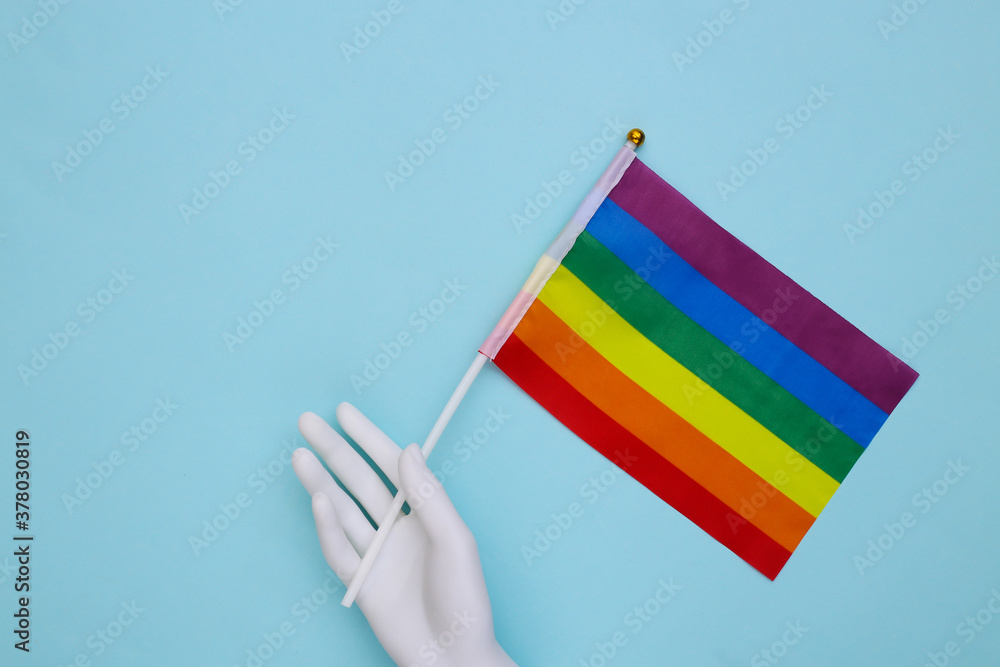 Fototapeta premium Mannequin hand holding LGBT rainbow flag on yellow background. Gay parade, freedom, tolerance