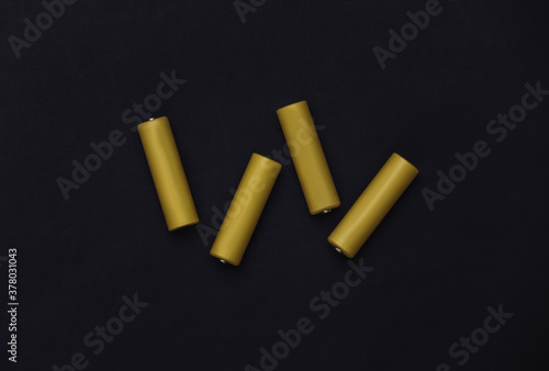 Four yellow AA batteries on black background. Top view