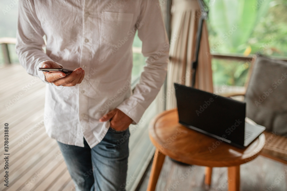 Cropped image man in white shirt using smaptphone, blurred laptop in the table on background Cropped image man in white shirt using smaptphone, blurred laptop in the table on background