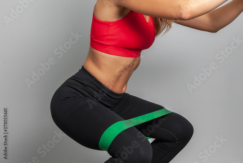 Slender woman in sportswear with fitness rubber bands on a gray background.