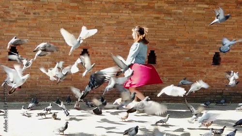 cute Chinese lady with a red dress and denim jacket, turning around herself happily with flying pigeons, and smiling to the camera, at Tha Pae Gate, Chiang Mai, Thailand. Slow-motion shot.