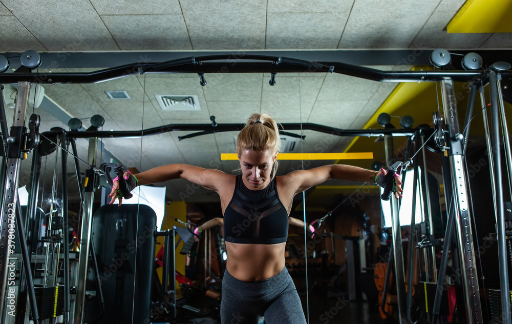 Young blond fit woman execute exercise with exercise machine Cable Crossover in gym. Workout process Young blond fit woman execute exercise with exercise machine Cable Crossover in gym. Workout process