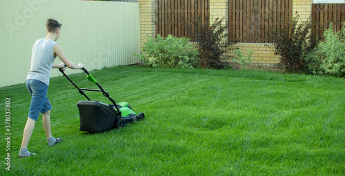 A teenager mows the lawn with a lawn mower.