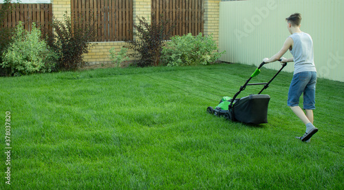 A teenager mows the lawn with a lawn mower. photo