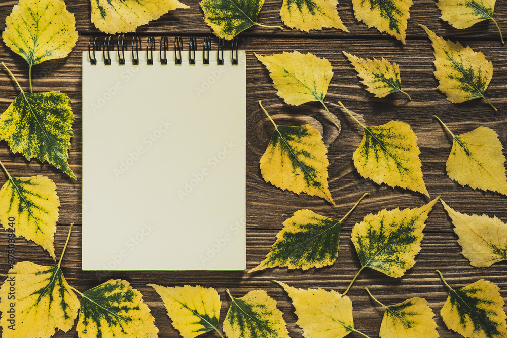 Notepad in a frame of yellow leaves on a wooden background. Creative flat lay autumn composition. Top view, copy space. - obrazy, fototapety, plakaty 