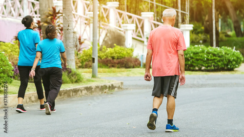 Back view portrait of a Asian elderly man in fitness wear walking and jogging for good health in public park. Senior jogger in nature.  Older Man enjoying Peaceful nature. Healthcare concept. © JinnaritT