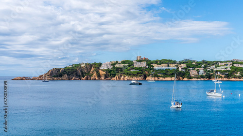 Sant Pol Beach with boats in the sea in a day with some white clouds.