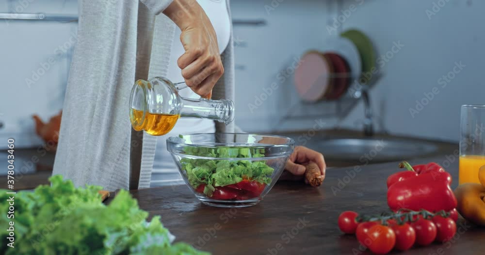 Cropped view of woman pouring oil in fresh salad in kitchen Cropped view of woman pouring oil in fresh salad in kitchen