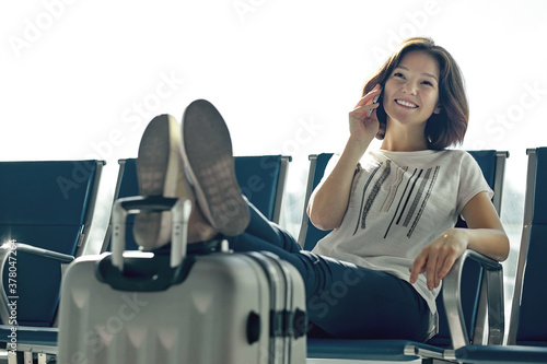 Air travel concept with young casual girl sitting with hand baggage suitcase. Airport woman talking on the phone at gate waiting in terminal.