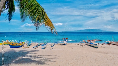 Traditional Filipino outrigger boats on a beautiful white sand beach  with turquoise water and blue sky in the resort area of Puerto Galera on the tropical island of Mindoro in the Philippines.