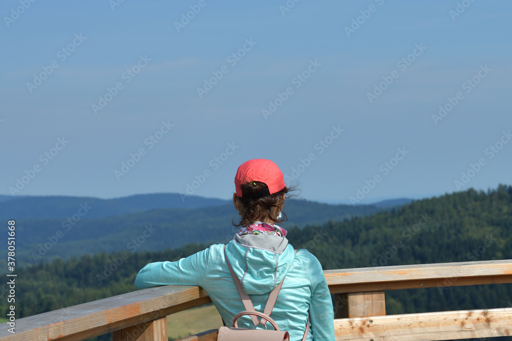 A teenage girl admires the surrounding nature from a tower during a pandemic in a hand on her face