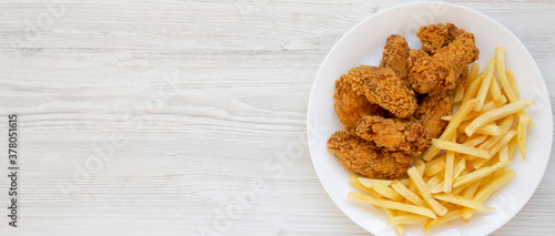 Homemade Crispy Chicken Wings and French Fries on a white plate on a white wooden background, overhead view. From above, top view, flat lay. Copy space.
