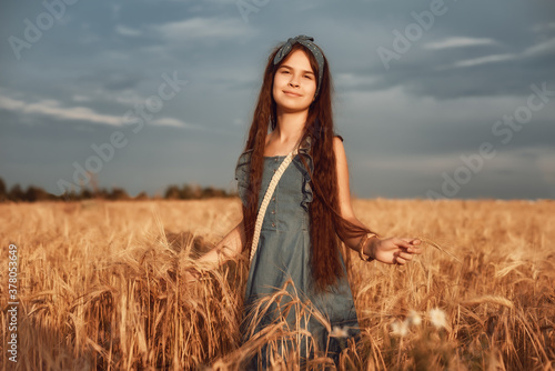 Portrait of Little girl 10-12 years old with long brown hair, walk in a wheat field on a summer evening © AstiMak