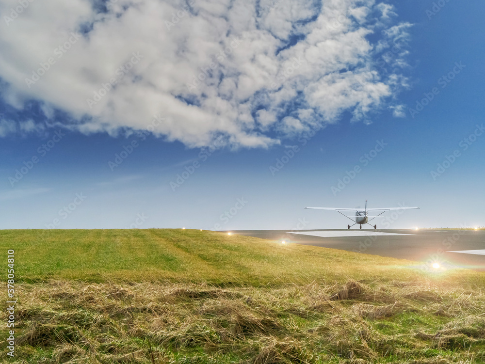 Single engine small airplane taking off a small run away. into cloudy sky. Bright run away lights are on. Short cut grass on a side. Single engine small airplane taking off a small run away. into cloudy sky. Bright run away lights are on. Short cut grass on a side.